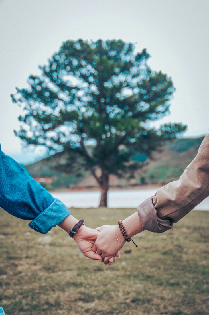 Two people holding hands outdoors, in front of a tree
