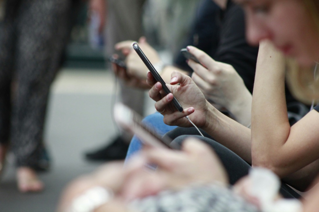 A row of people, each absorbed in their own phone